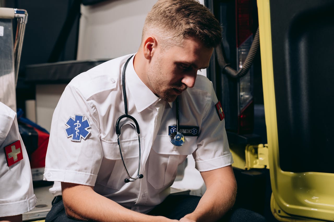 A paramedic in uniform sits pensively inside an ambulance, conveying healthcare dedication.